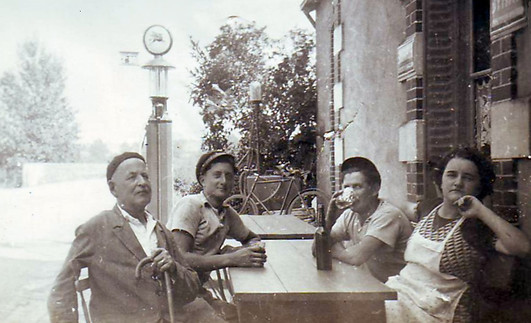 En terrasse, au café Gaudron. Au fond, on aperçoit la pompe à essence